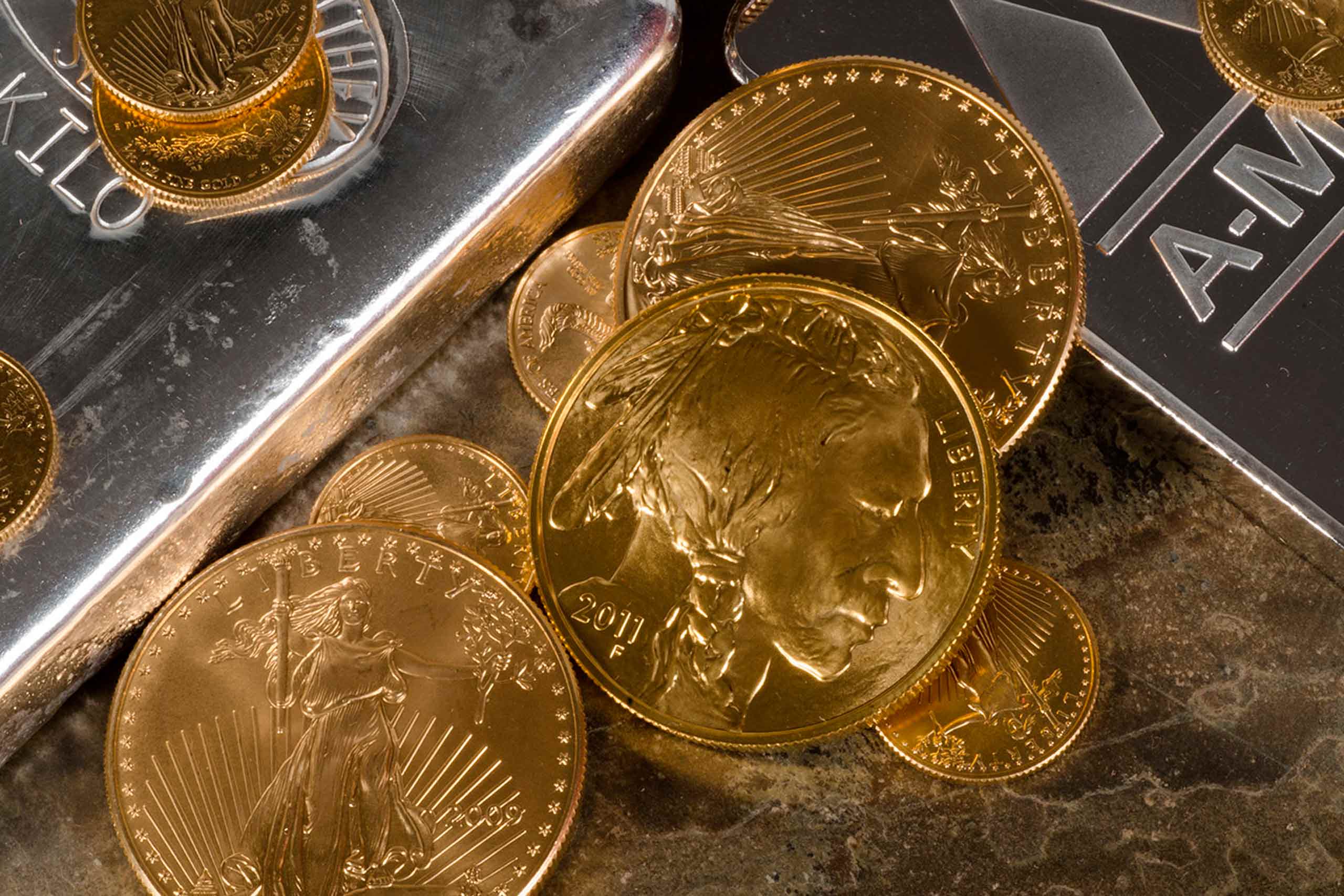 Fiscalidad metales preciosos — Varias monedas de oro apiladas sobre dos lingotes de plata